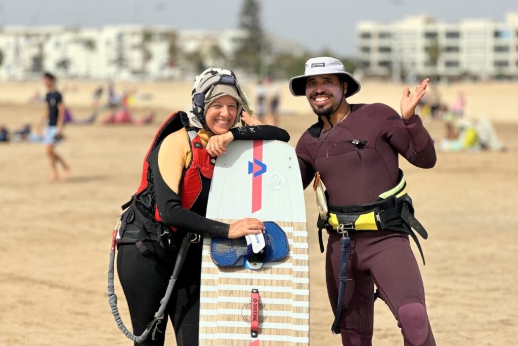 A kitesurf student and her instructor smiling on Essaouira beach, posing with a kiteboard after her first board lesson.