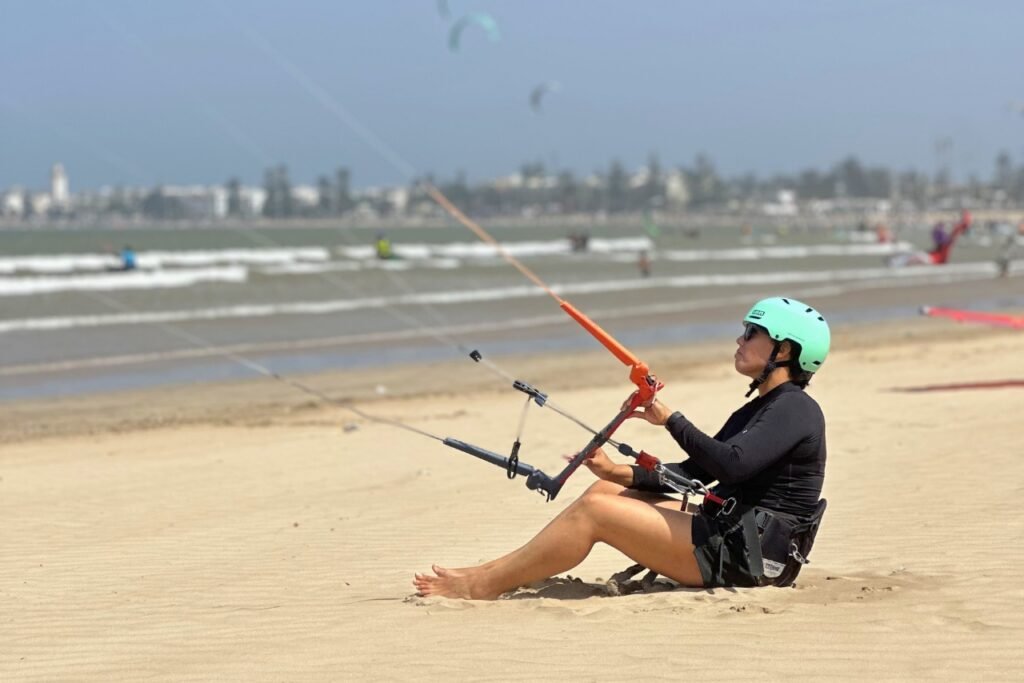 A beginner kitesurf student sitting on the sand in Essaouira, learning to control the kite during her first lesson.