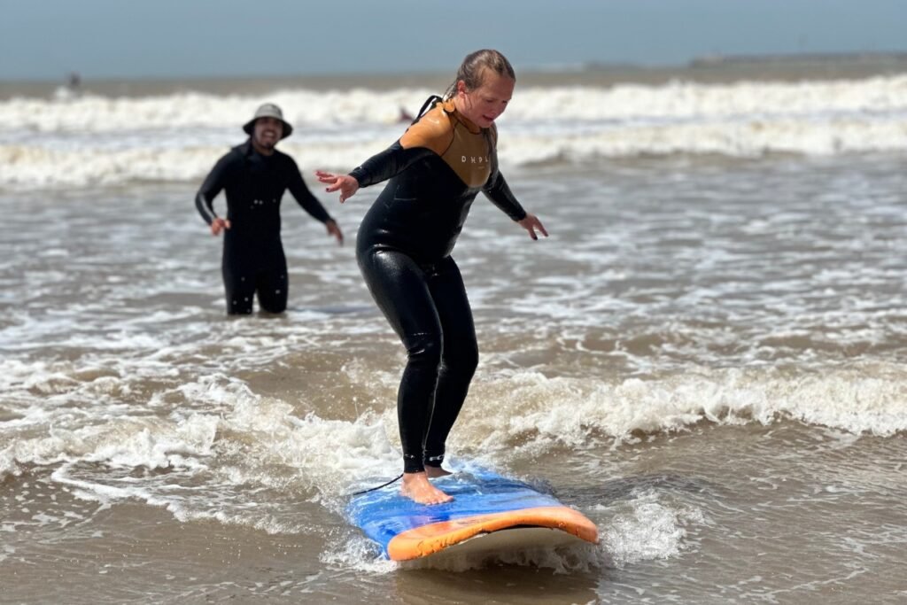 A beginner surfer standing on the surfboard in the lesson in Essaouira, with an instructor by her side.