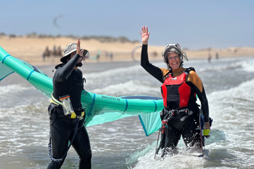 A private kitesurfing lesson in Essaouira - the student is waving and smiling while the instructor gives her a high-five.