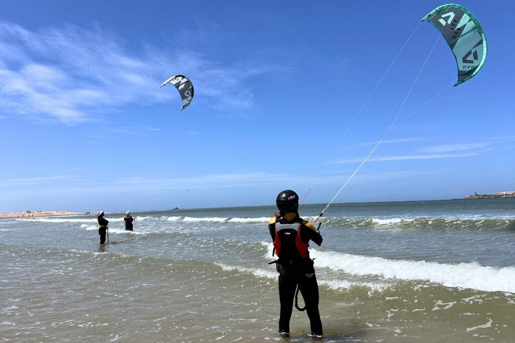 Two kitesurf students in the water with their instructor during a quiet shoulder season day on Essaouira beach.