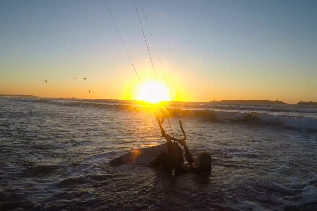 A kitesurf student preparing for a waterstart in Essaouira with a stunning winter sunset in the background.