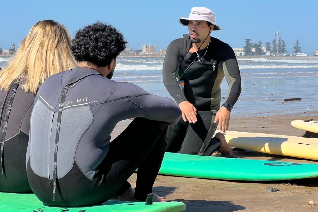 A surf instructor explaining theory to beginner students before their first surf lesson on Essaouira beach.